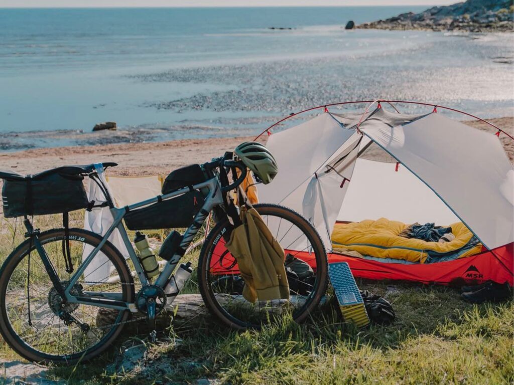 vélo devant une tente pour passer la nuit en face d'un lac en bikepacking