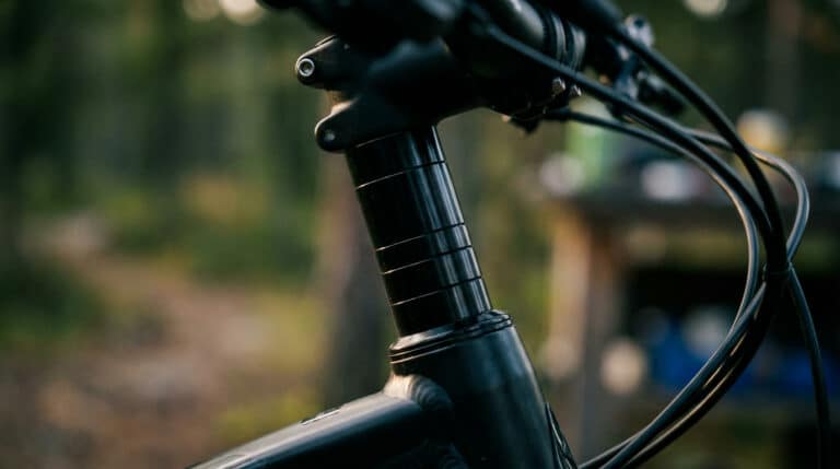 Détail d'un prolongateur de pivot de fourche de VTT noir, ajoutant de la hauteur. Bokeh extérieur vert/brun. Lumière naturelle. Suggère contrainte.